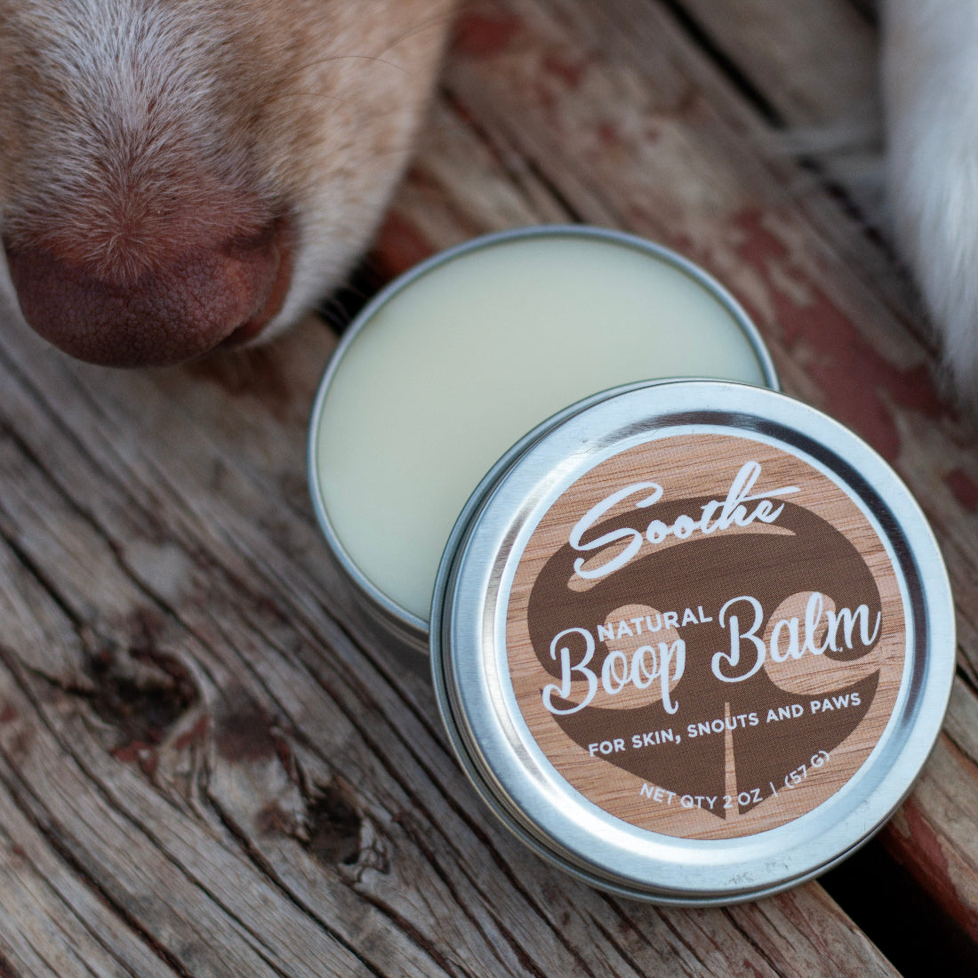Tin of Soothe Boop Balm with a dog's nose close by on a wooden surface