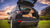 Labradoodle laying on voyager bed in the back of a black range rover SUV parked on grass with back door open in front of sunset